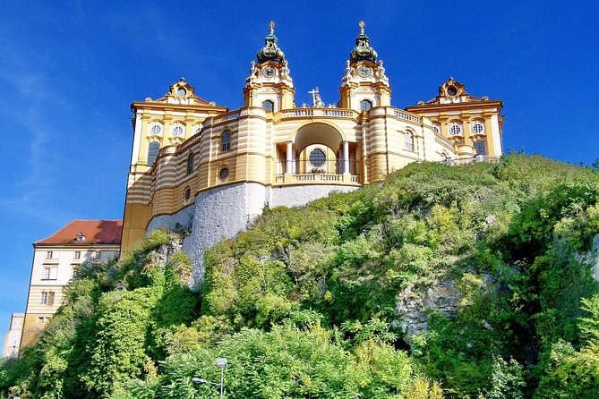 Melk Abbey's yellow and white facade on its wooded rock, seen from below
