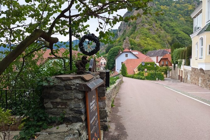 A village lane below steep green slopes, with a wreath on an old stone post